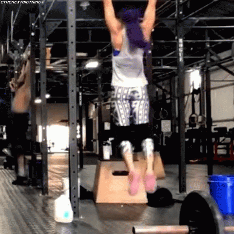A Woman With Purple Hair Is Doing Pull Ups In A Gym . GIF