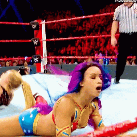 A Woman With Purple Hair Is Laying On The Ground In A Wrestling Ring GIF