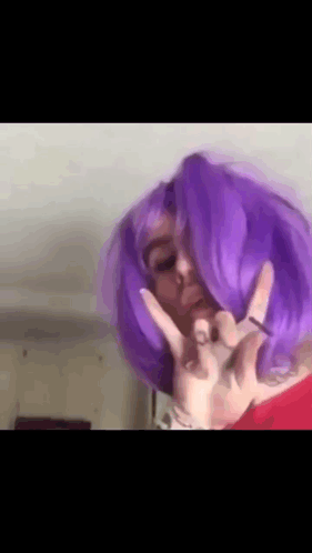 A Woman With Purple Hair Is Making A Peace Sign . GIF