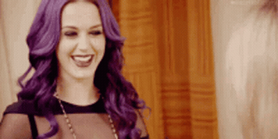 A Woman With Purple Hair Is Smiling And Wearing A Black Top And Necklace . GIF