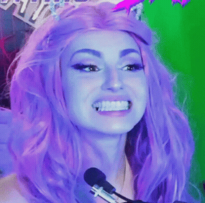 A Woman With Purple Hair Is Smiling In Front Of A Microphone While Wearing A Purple Wig . GIF