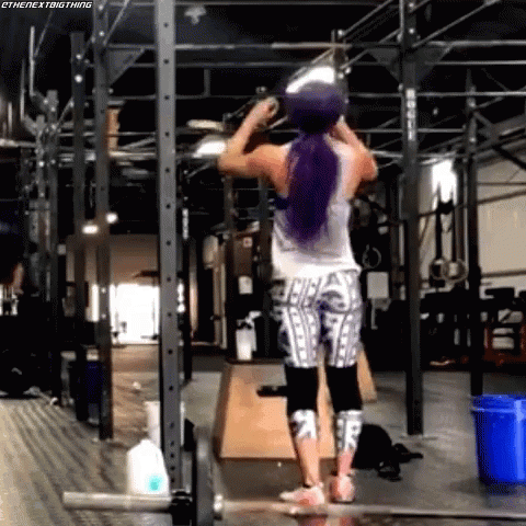 A Woman With Purple Hair Is Standing In A Gym Holding A Ball Over Her Head . GIF