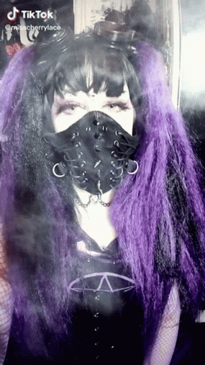 A Woman With Purple Hair Is Wearing A Black Face Mask GIF