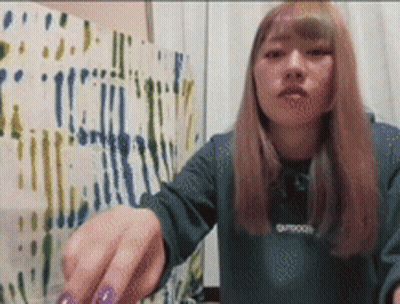 A Woman With Purple Nails Is Wearing A Green Sweater That Says Outdoor On It . GIF