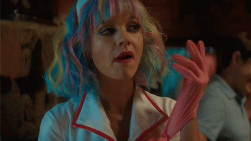 A Woman With Rainbow Hair Is Wearing A Nurse 'S Outfit And Holding A Pink Cotton Candy . GIF