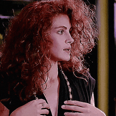 A Woman With Red Curly Hair Is Wearing A Black Shirt GIF
