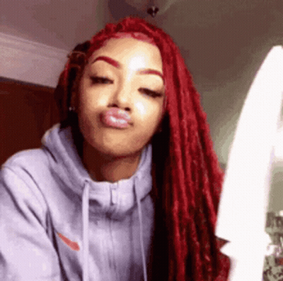 A Woman With Red Dreadlocks Is Wearing A Gray Hoodie And Making A Face . GIF