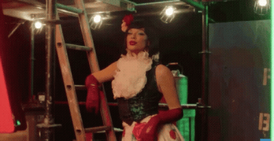 A Woman With Red Gloves And A Flower In Her Hair Is Standing Next To A Ladder GIF
