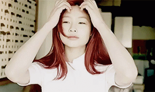 A Woman With Red Hair Adjusts Her Hair With Her Hands GIF