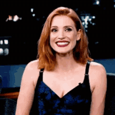A Woman With Red Hair And A Blue Dress Is Smiling . GIF