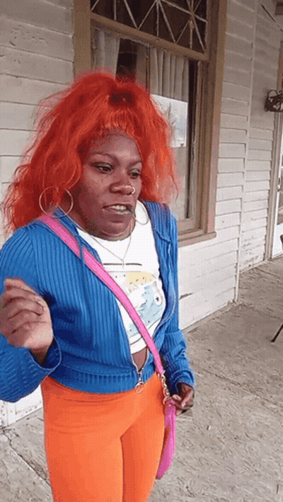 A Woman With Red Hair And A Pink Purse Stands In Front Of A Building GIF