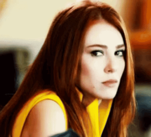 A Woman With Red Hair And A Yellow Shirt Is Looking At The Camera . GIF