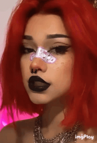 A Woman With Red Hair And Black Lips Is Wearing A Nose Ring And A Necklace . GIF