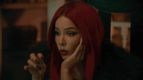 A Woman With Red Hair And Black Nails Holds Her Hand To Her Chin GIF