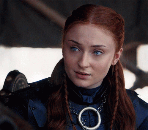 A Woman With Red Hair And Blue Eyes Is Wearing A Necklace With A Circle Around It GIF