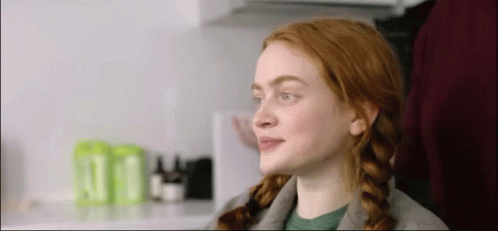 A Woman With Red Hair And Braids Is Sitting In A Chair In A Kitchen . GIF