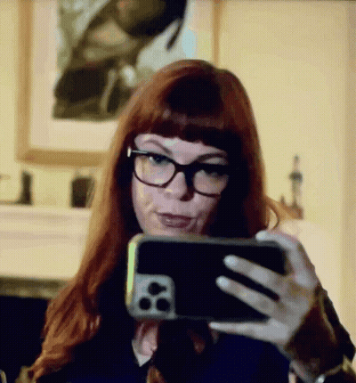 A Woman With Red Hair And Glasses Is Taking A Selfie With Her Cell Phone GIF