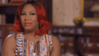 A Woman With Red Hair And Red Lipstick Is Sitting In A Chair In A Living Room . GIF