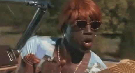 A Woman With Red Hair And Sunglasses Is Sitting In A Convertible Car . GIF