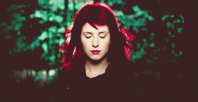 A Woman With Red Hair Has Her Eyes Closed In Front Of A Green Background GIF