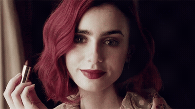A Woman With Red Hair Holds A Lipstick In Her Hand GIF