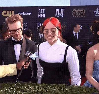 A Woman With Red Hair Is Being Interviewed By A Man In Front Of A Wall That Says Fiji Water GIF