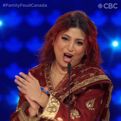 A Woman With Red Hair Is Clapping In Front Of A Microphone While Wearing A Red And Gold Outfit GIF