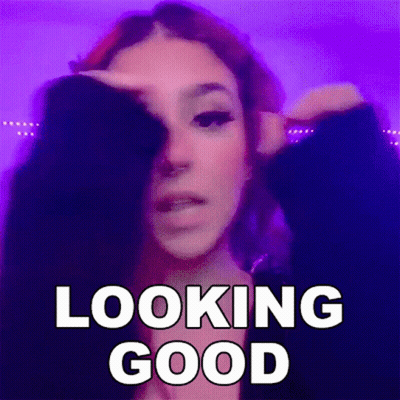 A Woman With Red Hair Is Covering Her Face With Her Hand And The Words `` Looking Good '' Written Above Her . GIF