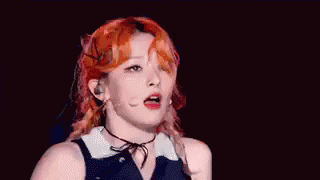 A Woman With Red Hair Is Dancing On A Stage With A Microphone In Her Hand . GIF