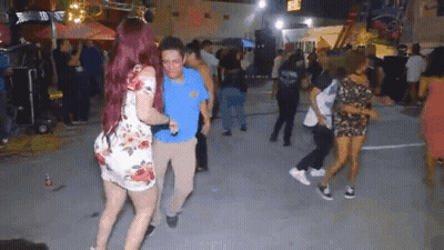 A Woman With Red Hair Is Dancing With A Man In A Blue Shirt In Front Of A Crowd Of People . GIF