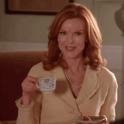 A Woman With Red Hair Is Drinking A Cup Of Tea And Holding A Plate Of Food GIF