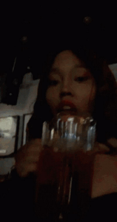 A Woman With Red Hair Is Drinking A Red Liquid From A Glass GIF
