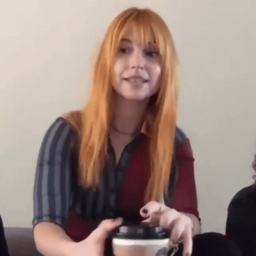 A Woman With Red Hair Is Holding A Cup Of Coffee In Her Hand . GIF