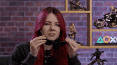 A Woman With Red Hair Is Holding A Pair Of Sunglasses GIF
