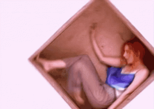 A Woman With Red Hair Is Laying In A Box GIF