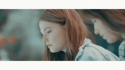 A Woman With Red Hair Is Looking Down At Something While Another Woman Looks At Her Reflection In The Mirror . GIF