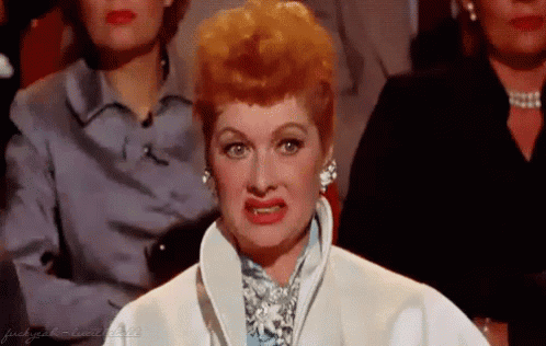 A Woman With Red Hair Is Making A Funny Face While Sitting In Front Of A Crowd Of People . GIF