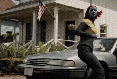 A Woman With Red Hair Is Running In Front Of A Car With A License Plate That Says Jfu725 GIF
