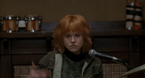 A Woman With Red Hair Is Singing Into A Microphone In Front Of A Sign That Says Ami On It GIF