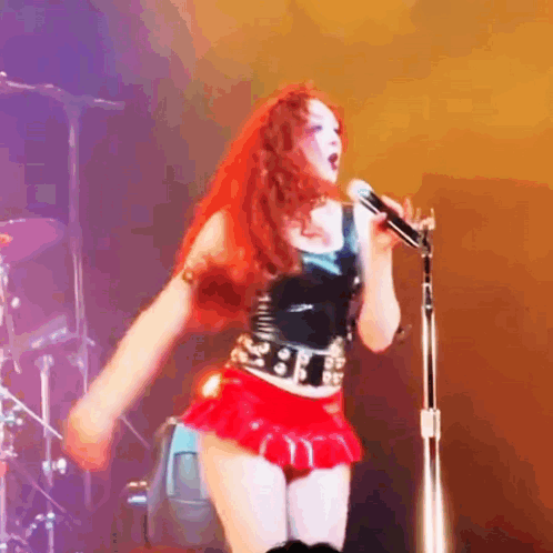 A Woman With Red Hair Is Singing Into A Microphone On A Stage . GIF