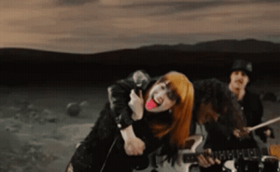 A Woman With Red Hair Is Singing Into A Microphone While A Man Plays Drums . GIF