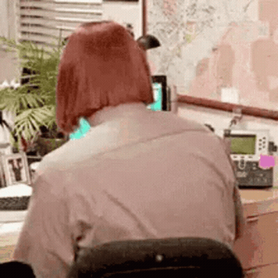 A Woman With Red Hair Is Sitting At A Desk In Front Of A Map . GIF