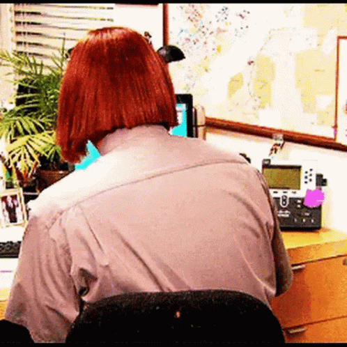A Woman With Red Hair Is Sitting At A Desk With A Telephone And A Computer . GIF