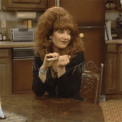 A Woman With Red Hair Is Sitting At A Table In Front Of A Dishwasher GIF