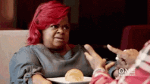 A Woman With Red Hair Is Sitting At A Table Talking To Another Woman . GIF
