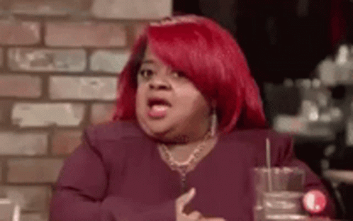 A Woman With Red Hair Is Sitting At A Table With A Glass Of Water In Front Of A Brick Wall . GIF