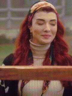 A Woman With Red Hair Is Sitting At A Table With Her Eyes Closed And Holding A Piece Of Wood . GIF