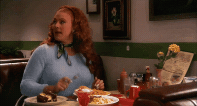 A Woman With Red Hair Is Sitting At A Table With Plates Of Food And A Menu GIF
