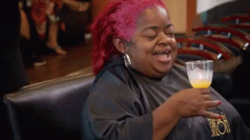 A Woman With Red Hair Is Sitting In A Chair Holding A Glass Of Orange Juice GIF