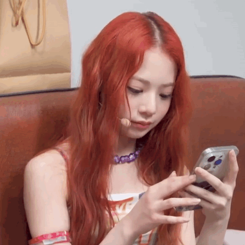 A Woman With Red Hair Is Sitting In A Chair Looking At Her Phone GIF